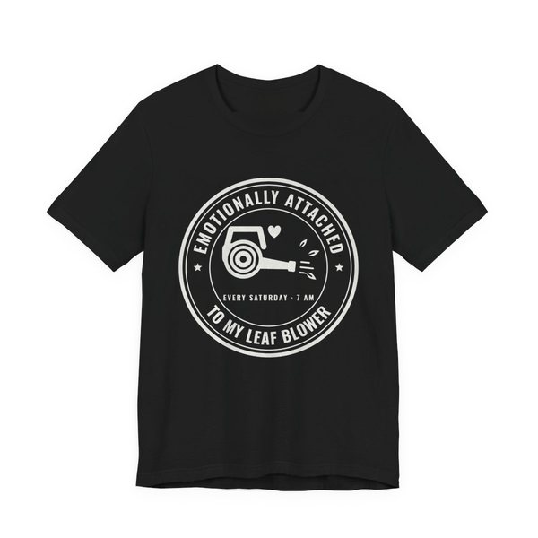 Black t-shirt printed in off-white ink with a round badge reading “Emotionally Attached to My Leaf Blower” around a leaf blower with a little heart, plus “Every Saturday · 7 AM”