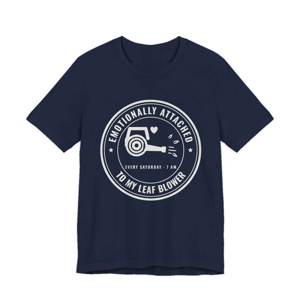 Navy t-shirt printed in off-white ink with a round badge reading “Emotionally Attached to My Leaf Blower” around a leaf blower with a little heart, plus “Every Saturday · 7 AM”