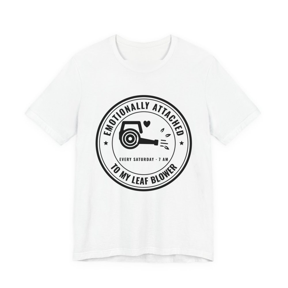 White t-shirt printed in dark ink with a round badge reading “Emotionally Attached to My Leaf Blower” around a leaf blower with a little heart, plus “Every Saturday · 7 AM”