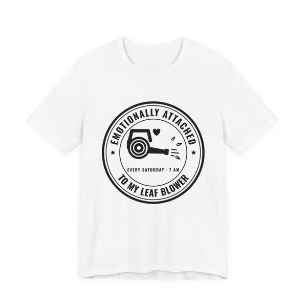 White t-shirt printed in dark ink with a round badge reading “Emotionally Attached to My Leaf Blower” around a leaf blower with a little heart, plus “Every Saturday · 7 AM”